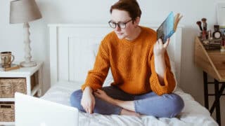 woman sitting on bed looking at laptop