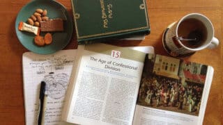 textbook, plate of snacks, notebook, and mug of tea sitting on table