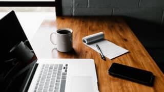 Laptop. coffee, notebook, and phone on desk