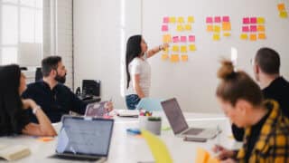 woman placing sticky notes on wall in front of coworkers