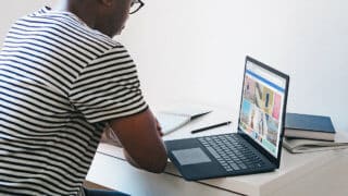 Man studying at table with notebook, pen, laptop, and books