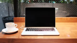MacBook on wooden table next to coffee cup and saucer