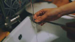 Person's hand washing a fork in a farmhouse sink