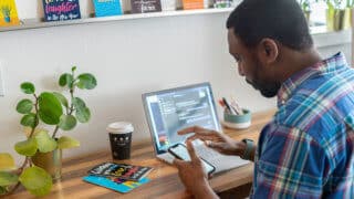 Man checking phone while working at laptop
