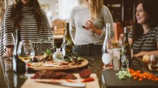 Three women cooking dinner and drinking wine
