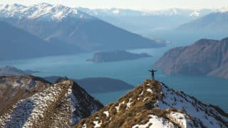 Person standing on snowy mountain summit with lake in background