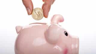Fingers putting coin into piggy bank