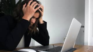 Stressed woman holding hands on head in front of laptop