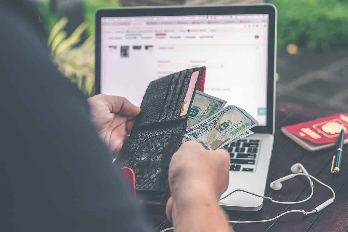 pulling bills out of wallet in front of laptop