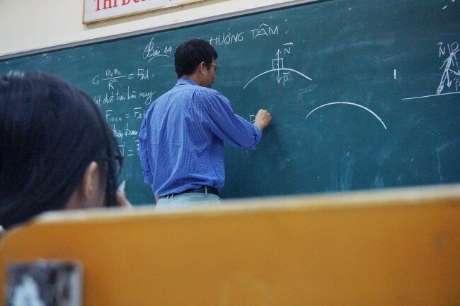 teacher writing physics problem on the board