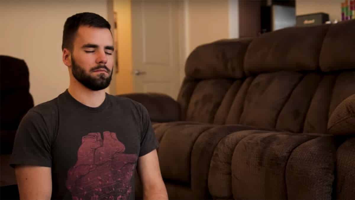 Bearded man meditating on the floor next to a couch