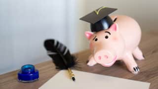 Piggy bank wearing graduation cap with quill pen and inkwell