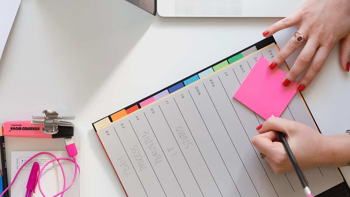 Person writing on pink sticky note