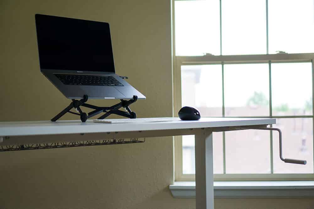 IKEA standing desk with mouse, keyboard, and MacBook on laptop stand