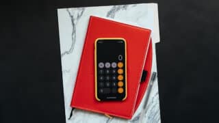 iPhone showing calculator app on top of red notebook and marble folder