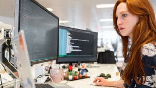 Software developer coding at desk with dual monitors