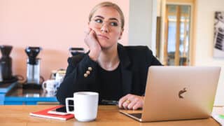 Bored woman sitting at desk with coffee cup and MacBook