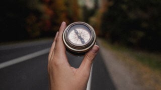 Hand holding compass in front of roadway