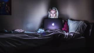 Woman sitting in bed under covers and staring at MacBook