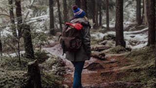 Woman with backpack hiking through forest with light snow on the ground