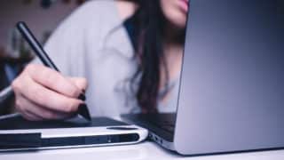 Closeup of woman drawing on tablet next to a laptop