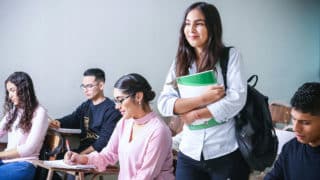 Woman walking into classroom with green textbook