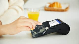 Hand swiping credit card in machine in front of glass of orange juice and pastry