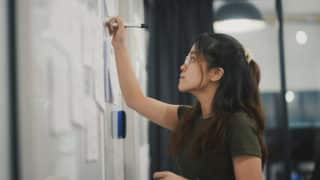 Woman writing on a whiteboard with a dry eras marker next to sticky notes